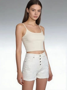 Detail of high-waist white denim shorts with four-button closure and distressed ripped hem