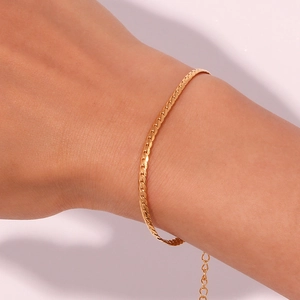 Detailed close-up of a delicate 18K gold-plated snake chain bracelet on a woman's wrist
