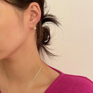 Elegant gold knot stud earrings with white pearls worn by a model in a cozy setting