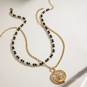Double-layered gold necklace with pearls, black beads, and a sun-eye zircon pendant