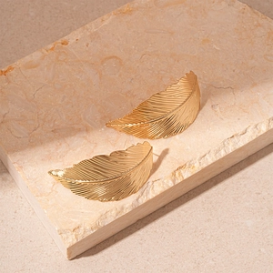 Close-up of golden metal leaf earrings with intricate feather textures on stone