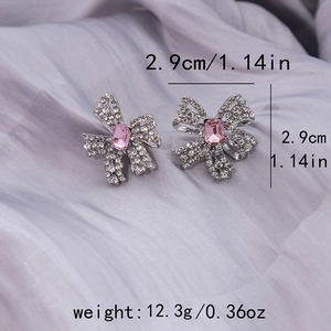 Close-up of bow earrings with pink crystal and white pavé stones on silk cloth