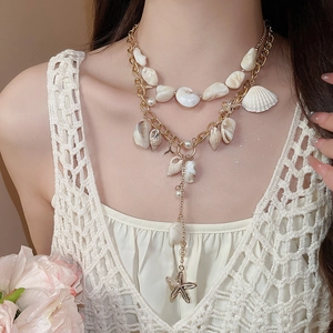 Detail of layered gold necklace with natural shells, starfish, and pearl pendants on model