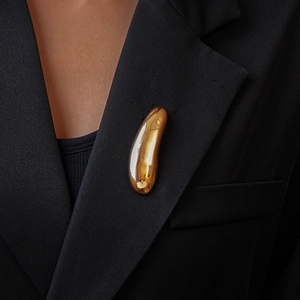 Polished gold metal drop brooch accessory worn on a black suit lapel for a modern style