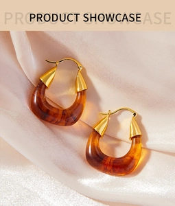 Detail of amber resin U-shaped earrings on pink satin background showing golden metal finish