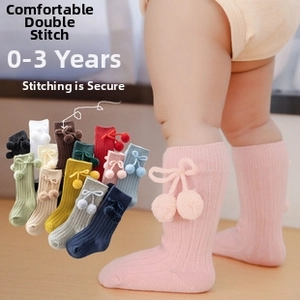 Detailed knit texture of baby knee-high socks with pom-pom and bow accents