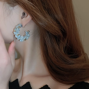 Close-up of C-shaped earrings with light blue natural stones worn by a model