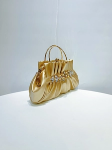 Detailed view of the gold evening clutch with pleated texture and rhinestone ornament