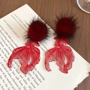 Macro shot of dark red hollow koi fish pendant earrings with plush balls on a book