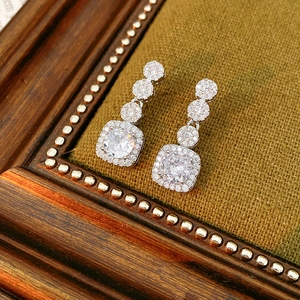 Close-up of square zircon drop earrings on olive green velvet inside a vintage frame