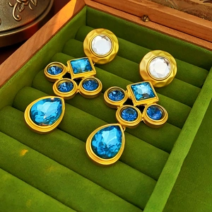 Close-up of vintage gold earrings with blue and clear gems in a green velvet box