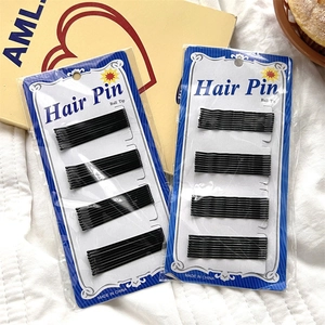 Detail of wavy black bobby pins with ball tips on packaging over quilted fabric