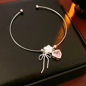 Macro detail of silver bangle with pink heart gemstone, star charm and bow pendant
