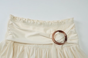 Detail view of cream skirt waistband with elastic pleats and decorative brown resin ring