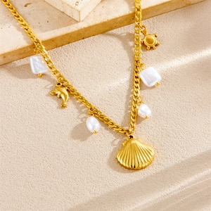 Gold stainless steel ocean bracelet with shell, dolphin and pearl charms on stone surface