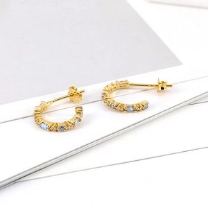 Macro detail of gold C-shaped earrings with inlaid sky blue and white zircon stones