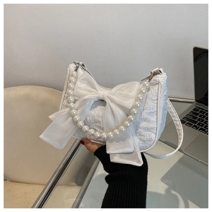Close-up of white textured handbag with organza bow and imitation pearl handle strap