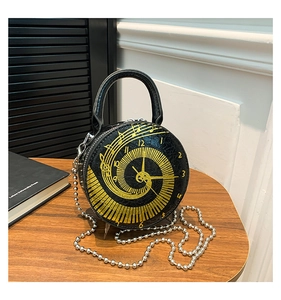 Detail of black round handbag with crocodile texture and gold clock pattern on desk