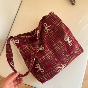 Détail du sac cabas en tweed à carreaux rouges avec broderie nœud blanc et étiquette latérale
