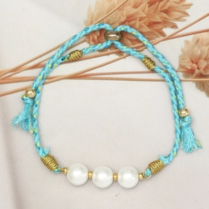 Detailed shot of blue braided rope bracelet with three white faux pearls and gold beads