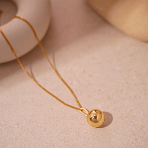 Vue macro détaillée d'un collier pendentif sphère dorée sur une surface en pierre épurée