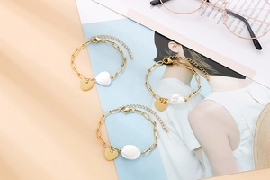 Détail de bracelets chaîne trombone dorés avec pendentif cœur et perle blanche ovale