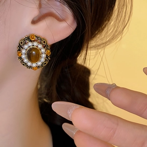 Macro view of vintage style oval tiger eye and pearl earrings worn by a model