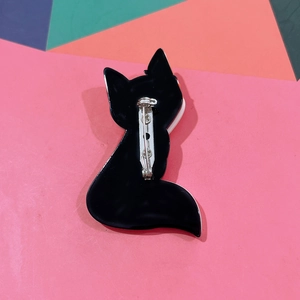 Detail view of the back of black acrylic fox brooch with silver pin on colorful background