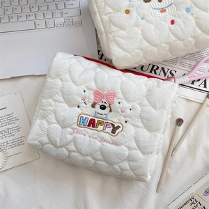 Detail of heart-quilted puppy makeup bag with embroidery and zipper closure on a desk