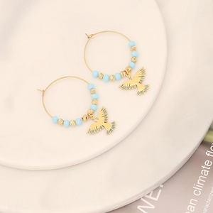 Gold hoop earrings with blue beads and peace dove pendants on a white porcelain plate