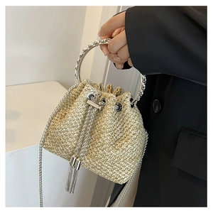 Detail of a beige woven straw bucket bag with silver metal handle and fringe tassels