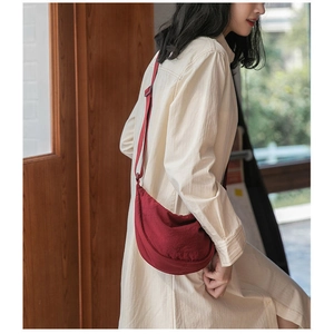 Detail of red crescent crossbody bag in nylon fabric worn by model in a natural setting