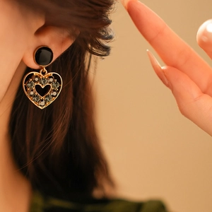 Gros plan de boucles d'oreilles cœur dorées avec clous noirs et strass gris sur mannequin