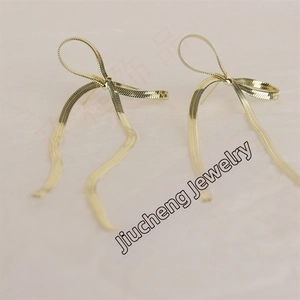 Detailed close-up of golden bow-knot stud earrings featuring textured snake chain design