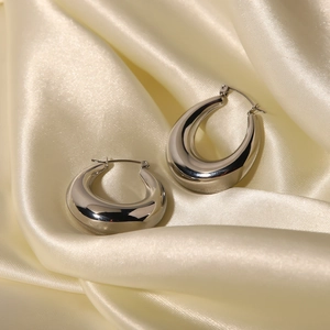 Macro shot of polished silver teardrop earrings on elegant beige silk fabric background