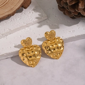 Detailed view of golden heart earrings with hammered texture on a natural stone surface
