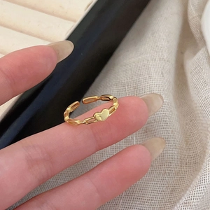Gold heart ring with chain-link band on model's finger in warm lighting