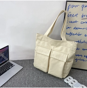 Detail of off-white canvas tote bag featuring functional front pockets and fabric texture