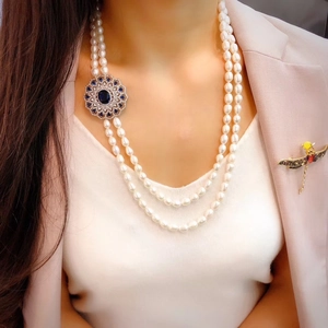 Detail of double-layer pearl necklace with blue gemstone pendant and dragonfly brooch