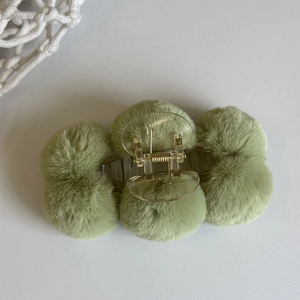 Close-up of a green plush ball hair claw clip with transparent plastic and gold spring
