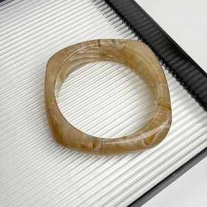Detail of square amber resin bracelet featuring marble fluid texture on a white tray