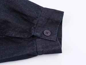 Nahaufnahme der dunkelblauen Denim-Jackenmanschette mit Harzknopf und Twill-Textur