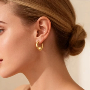 Close-up of a gold-plated stainless steel hoop earring with a polished bead on model's ear