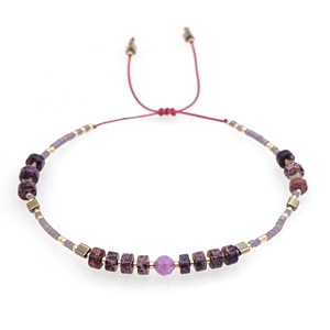 Handmade beaded bracelet with purple patterns, golden cubes, and pink focal stone