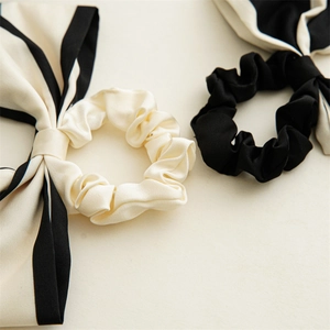 Close-up of elegant satin bow hair scrunchies in cream and black with contrast piping
