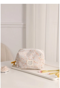 Detailed view of beige tweed cosmetic bag on white tray with makeup brushes and floral decor