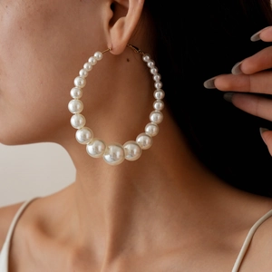 Close-up of elegant gold hoop earrings with gradient white pearls on a female model