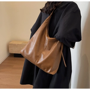 Detailed view of the brown soft leather tote bag worn by a model in casual black outfit