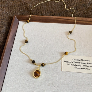 Retro tiger eye stone necklace with gold chain and zircon pendant on a beige jewelry tray