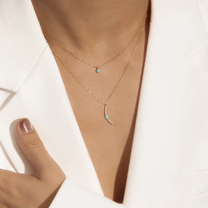 Detail of layered gold necklace featuring turquoise moon and circle pendants on a model